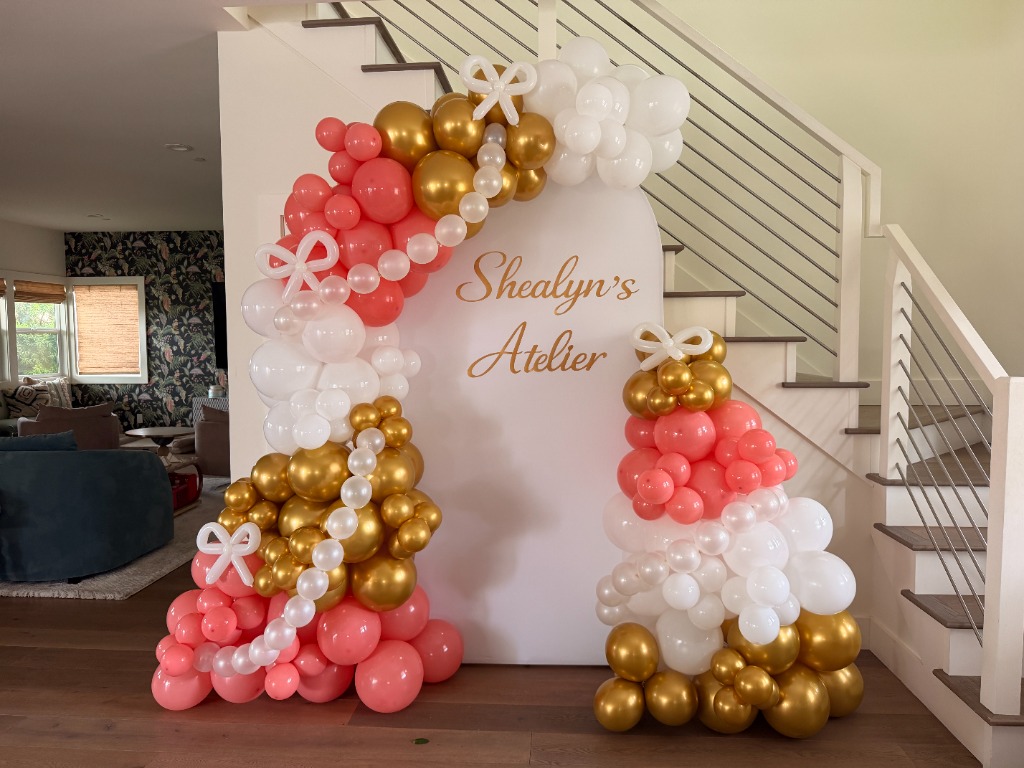Elegant balloon decor with coral, white, and gold balloons on a custom arch backdrop