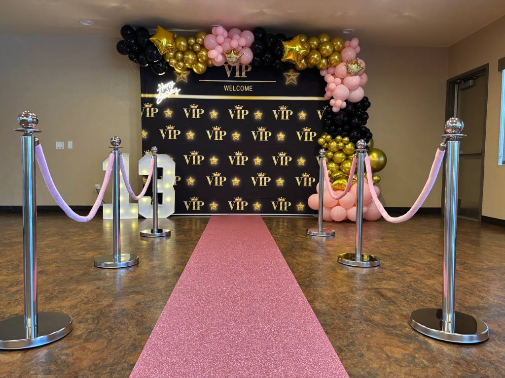 VIP 13th birthday party setup with red carpet, stanchions, and black, gold, and pink balloon garland